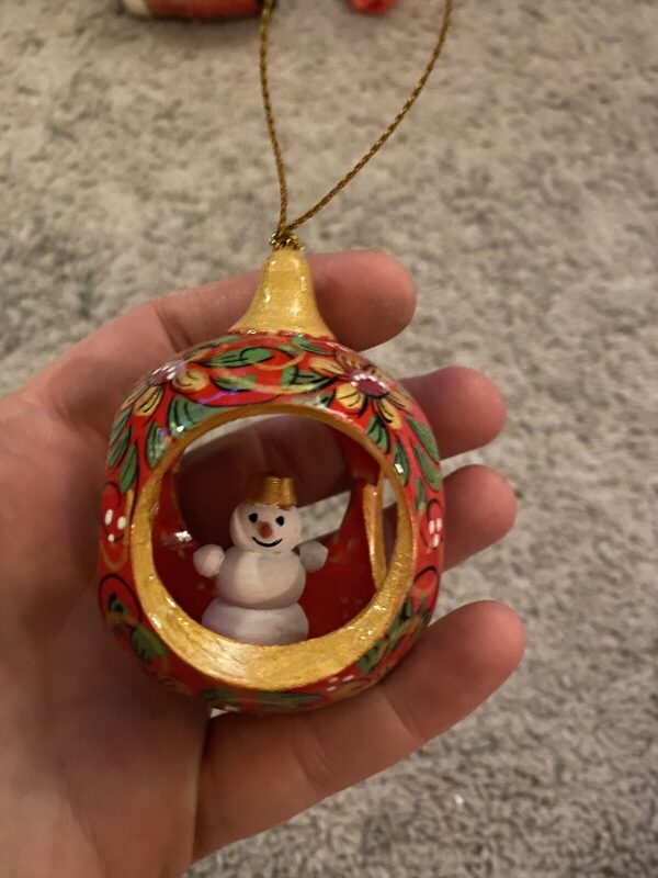A turned and painted wood ornament, cut open to a little snowman inside, in red-and-gold folk florals