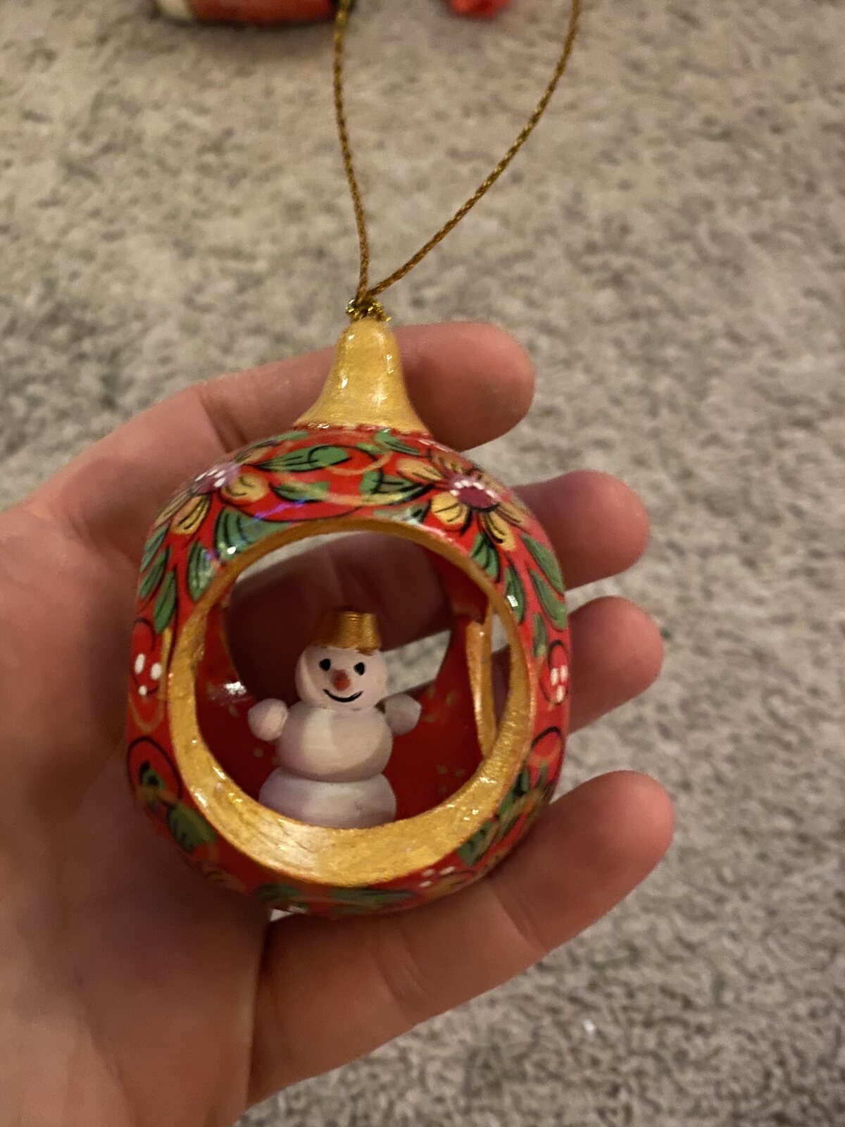 A hand-painted diorama ornament ball, opened to its snowman scene, held in the hand